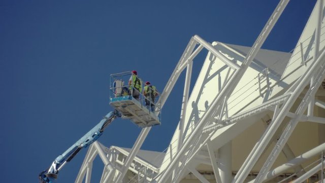 Delay on the wall. Painting a new building. Sky lift. Two painters in the cradle of the elevator are painted with yellow paint on the walls of the old building.