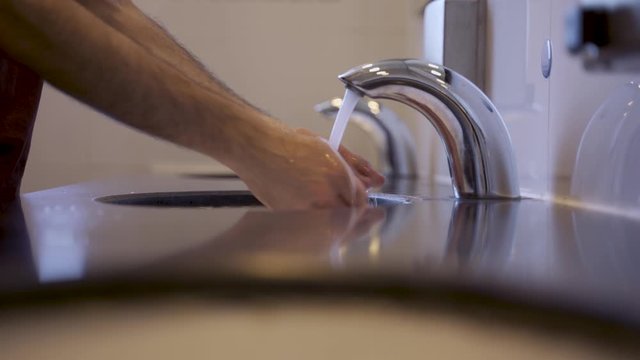 Man washing hands in public toilets with touch-less faucet or tap