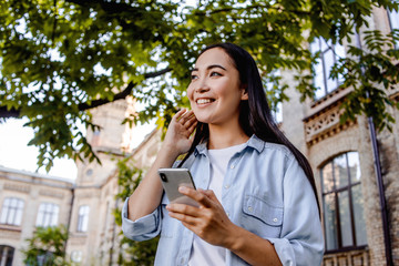 Fototapeta premium Beautiful japanese woman call for friend, with mobile cell phone in hand, smile and looking away. Walk alone, travel in new city, using mobile app with offline maps.