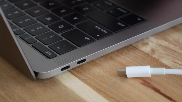 Male hand typing on keyboard and plugging in a white power USB-C or Type C Cable into a laptop computer's USB-C port. Thunderbolt connector. Closeup. 4k