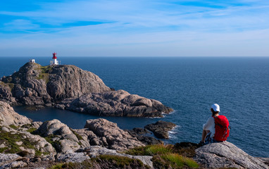 Fototapeta na wymiar girl with red backpack doing walking on the lighthouse of Lindesnes, Norway