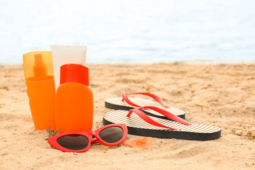 Sunscreen cream with flip-flops and sunglasses on sand beach