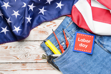 Jeans with tools in pocket, USA flag and card on wooden background. Labor Day celebration