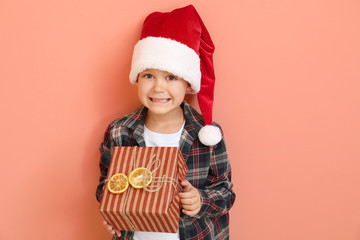 Little boy in Santa hat and with Christmas gift on color background