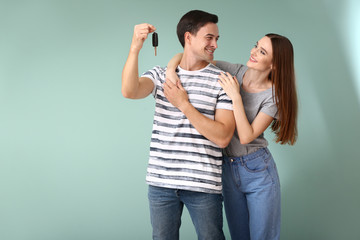 Fototapeta premium Happy couple with key from their new car on color background