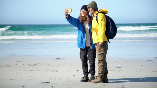 Two young women travelers are taking a selfie with a smartphone on the beach of Lofoten islands, Norway.