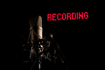Mikrofon im dunklen Studio vor roter Recording Leuchtschrift im Hintergrund