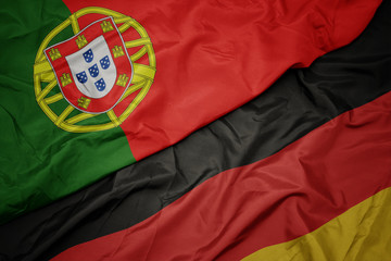 waving colorful flag of germany and national flag of portugal.