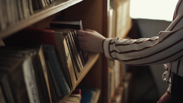 Close up of female hands looking for a book from a bookshelf in library