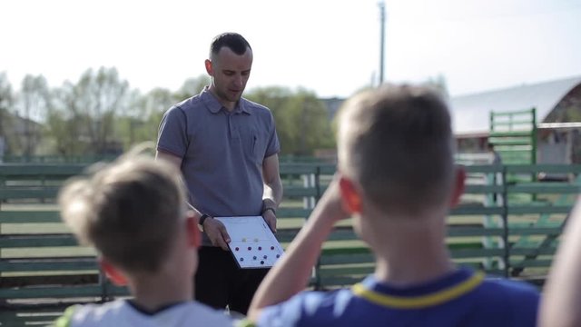 Young Football coach trainer coaching kids using tactic strategy magnetic whiteboard. Soccer trainer explaining match tactics to children soccer team.