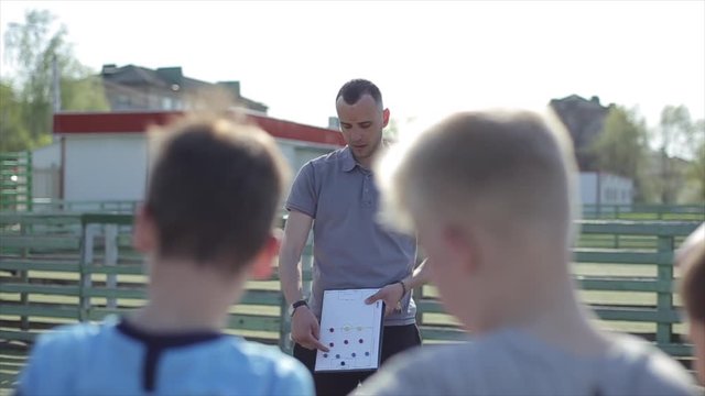 Young Football coach trainer coaching kids using tactic strategy magnetic whiteboard. Soccer trainer explaining match tactics to children soccer team.