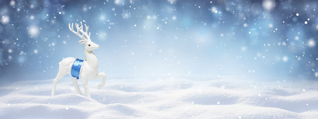Winter snow background with snowdrifts, with beautiful light and snow flakes on the blue sky in the evening, banner format, copy space.