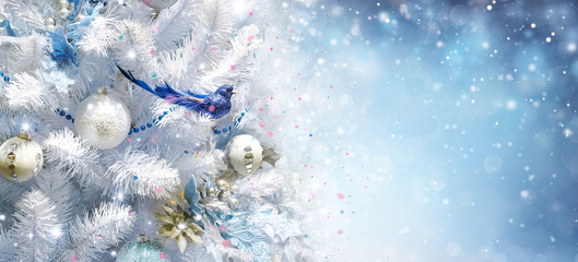 White Christmas tree decorated with silver golden Christmas balls and beautiful blue bird good luck on sparkling and fabulous fairy blue evening sky with falling snow with beautiful bokeh, copy space.
