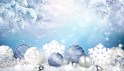 Festive Christmas decorative composition with blue and white balls, snowflakes in the snow and snow covered fir branches on background of falling snow. Copy space.