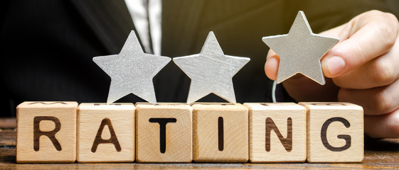 Businessman puts the third star above the word Rating on wooden blocks. The concept of quality of...