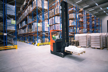 Worker operating forklift machine and relocating goods in large warehouse center.