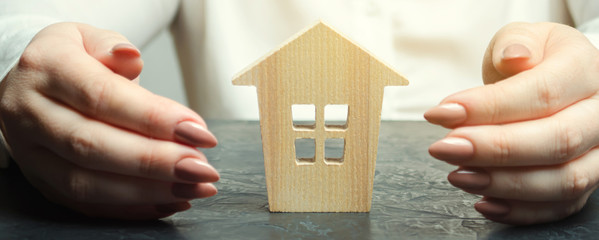 A woman is protecting a miniature wooden house. Property insurance concept. Protection of housing....