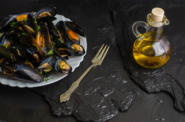 Delicious cooked seafood mussels with herbs and olive oil on a white plate on black background. Mediterranean cuisine