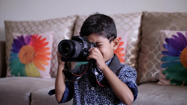 Young Indian kid clicking photographs on his digital camera DSLR - Learning photography at home. A 5-year-old school going kid learning photography at home and trying to click pictures - Technology...