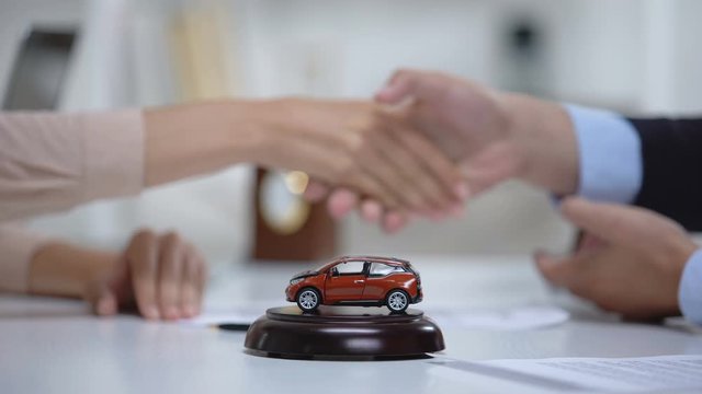 Car toy on table, woman signing vehicle purchase or insurance on background