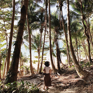 A young woman in brown skirt, white shirt and black straw hat standing in jungle with a lot of exotic palm trees. Tropical, summer, travel and vacation concept.
