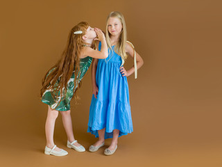 Beautiful red-haired girl with long hair in a green dress whispers in the ear of a girl with long...
