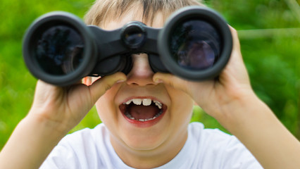 curious boy looks for wildlife through binoculars in the park.Exploring the world. Summer holidays. Outdoor activities.