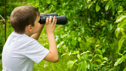 curious little boy looking up through binoculars. Exploring the world. Summer holidays. Outdoor activities.
