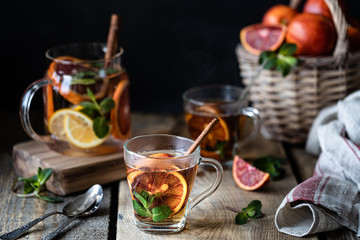 Homemade tea in a transparent glass with red orange and lemon, cinnamon and mint on a wooden background. Oranges Wicker Basket