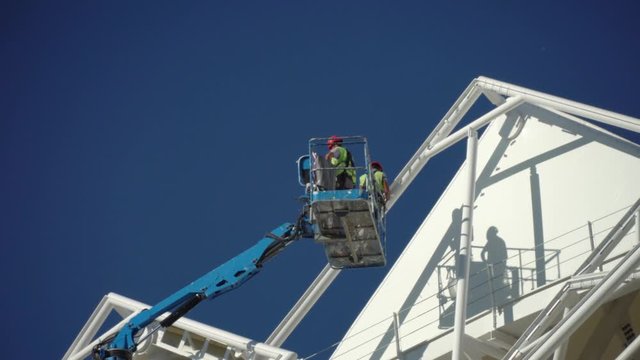 Delay on the wall. Painting a new building. Sky lift. Two painters in the cradle of the elevator are painted with yellow paint on the walls of the old building.
