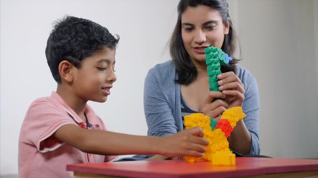 Low angle shot of an Indian mother and child playing with colourful building blocks. A young Indian single mother and her little child is playing with blocks at home. Fun learning at home with new ...