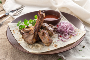 Grilled lamb ribs on lavash bread with red onion and tomato sauce on tablecloth
