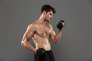 Handsome young strong sportsman posing isolated over grey wall background make exercises with...