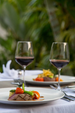 Beefsteak With Steamed Vegetables And Glasses Of Red Wine Served On The Table, Romantic Dinner Outdoor 