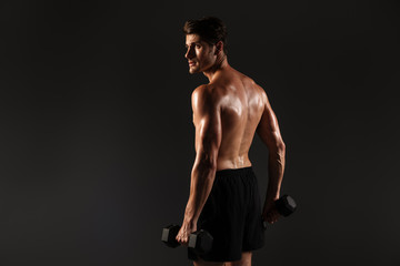 Fototapeta na wymiar Concentrated handsome young strong sportsman posing isolated over black wall background holding dumbbells.