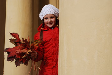 girl in a white hat and a red jacket in autumn with a bouquet of autumn maple leaves in her hands