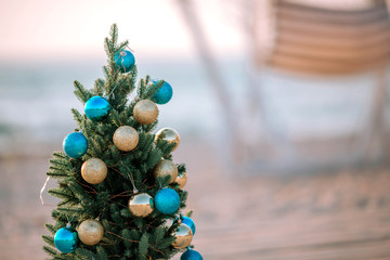 Christmas tree decorated with gold and blue balls on a sea sandy beach.