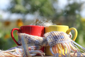 red and yellow mugs wrapped in a scarf on a garden background in the afternoon. joint warming breakfast in the garden