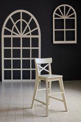 White chair on dark background.The wall is decorated with details in the form of arched doors and arched Windows.