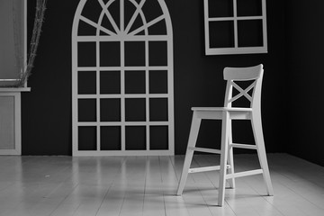 Naklejka premium White chair on dark background.The wall is decorated with details in the form of arched doors and arched Windows.