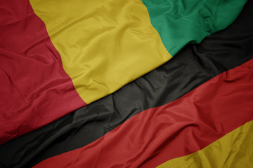 waving colorful flag of germany and national flag of guinea.