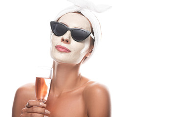 woman in sunglasses and cosmetic hair band with facial mask holding wine glass isolated on white
