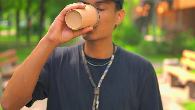 cheerful young man drinking coffee to go in summer city park trendy guy holding cup with drink outdoors