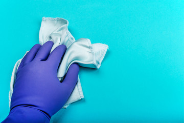 hand in a rubber glove holding a rag and wipes on a blue background. the concept of cleaning an...