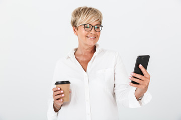 Portrait of smiling adult woman wearing eyeglasses holding cellphone and takeaway coffee cup