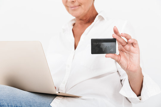 Image of caucasian adult woman wearing eyeglasses holding credit card while sitting with laptop computer