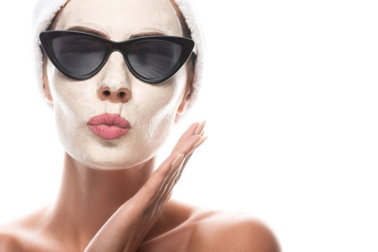front view of nude woman in sunglasses with facial mask making kissing face expression isolated on white