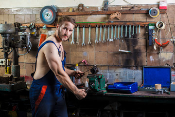 Auto mechanic repairs a detail clamped in a vise. Professional car mechanic working near table with different instruments and keeping in his hand spark plug from auto engine.