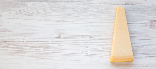 Piece of parmesan cheese on a white wooden surface. Top view, flat lay, from above. Space for text.