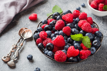 Fresh raspberries and blueberries in plate on dark background. Copy space.